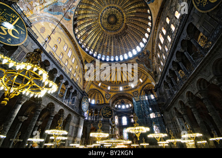 Hagia Sophia Inior Dome Kronleuchter Istanbul Türkei // ISTANBUL, Türkei — die große Haupthalle der Hagia Sophia zeigt ihre bemerkenswerte byzantinische Architektur mit ihrer massiven zentralen Kuppel, die von Pendentiven und Halbkuppeln gestützt wird. Das Innere zeigt sowohl christliche als auch islamische Elemente, darunter byzantinische Mosaike, osmanische Kalligrafie und große osmanische Vogelleuchter. Massive Marmorsäulen und -Tafeln säumen den Raum und demonstrieren die Pracht der architektonischen Technik aus dem 6. Jahrhundert. Stockfoto