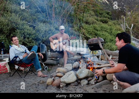 Drei Freunde sitzen um ein Lagerfeuer im Rincon Beach State Park in der Nähe von Carpinteria, Kalifornien. Stockfoto