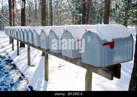 Eine Reihe von Schnee abgedeckten Mailboxen gegen einen bewaldeten Hintergrund. Stockfoto