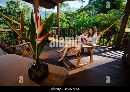 eine Mädchen sitzt auf einem Stuhl liest ein Buch auf dem Deck einer Kabine in Chiapas, Mexiko. Stockfoto