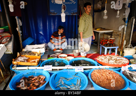 ISTANBUL, Türkei – Ein Händler stellt frischen Fisch und Garnelen in Kübeln zum Verkauf auf dem Karakoy Fish Market in der Nähe der Galata Brücke in Istanbuls historischem Uferviertel aus. Der traditionelle Markt serviert sowohl lokale Kunden als auch Restaurants, die täglich Fänge vom Bosporus und dem Schwarzen Meer anbieten. Stockfoto