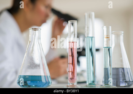 USA, New Jersey, Jersey City, Wissenschaftlerin Mikroskop hinter Reagenzgläser und Kolben Stockfoto