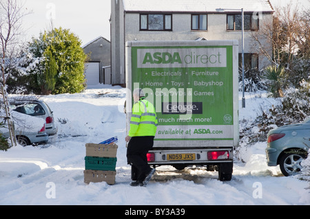 UK, Großbritannien. ASDA Hause Lieferwagen und Mann vor einem Haus liefern, Online-shopping mit Schnee in Wohnstraße im winter Stockfoto