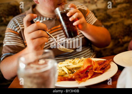 La Grange, California, Vereinigte Staaten von Amerika.  Ein Teenager nippt auf ein Soda beim Essen eines Teller mit Nudeln und Speck. Stockfoto