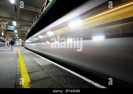Hochgeschwindigkeitszug auf der Durchreise einer fast menschenleeren Bahnhof Bahnsteig nachts Lichtstreifen zu schaffen. Stockfoto