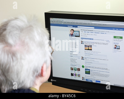 Ältere Frau mit Internet in diesem Fotografen business Seite auf Facebook Social Media zu suchen Website Webseite auf einem Computer zu Hause. England Großbritannien Stockfoto