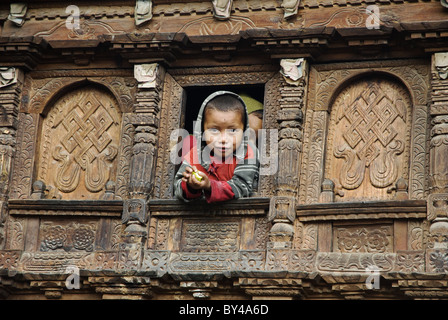 Ein Tamang junge Uhren aus einem Fenster in einem kunstvoll geschnitzten hölzernen Haus, Gatlang, Tamang Heritage Trek, Nepal Stockfoto