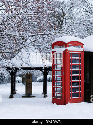 Traditionelle rote Telefonzelle mit Schnee auf einem englischen Dorfgrün Stockfoto