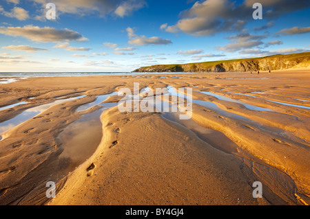 Fußspuren im Sand hinterlassen Surfer am Strand entlang hetzen und fangen die letzten Wellen vor Sonnenuntergang in Holywell Bay Stockfoto