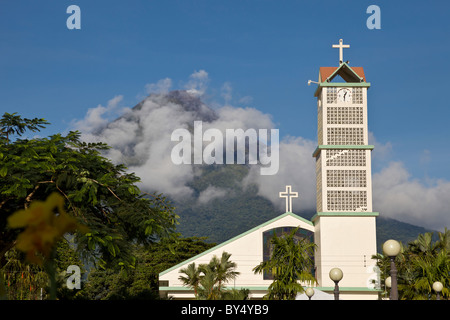 Wolken verdunkeln den drohenden Vulkan Arenal hinter der Kirche Zentralkirche in La Fortuna de San Carlos, Alajuela, Costa Rica. Stockfoto