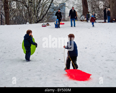 Kinder Schlitten hinunter einen Hügel im Central Park in New York City, nach einem schweren Schneesturm. Beachten Sie Manhattan Gebäude Hintergrund Stockfoto