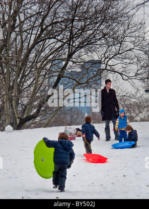 Kinder Schlitten hinunter einen Hügel im Central Park in New York City, nach einem schweren Schneesturm. Beachten Sie Manhattan Gebäude Hintergrund Stockfoto