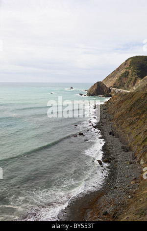 Wellen gegen die Felsenküste in Big Sur mit Big Creek Bridge entlang der kalifornischen Pacific Coast Highway, Kalifornien, USA. Stockfoto