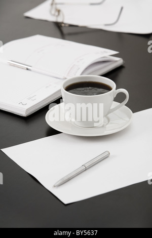 Morgen am Arbeitsplatz: Tasse Kaffee, Papiere, Notebook, Stifte, Gläser auf dem Tisch Stockfoto