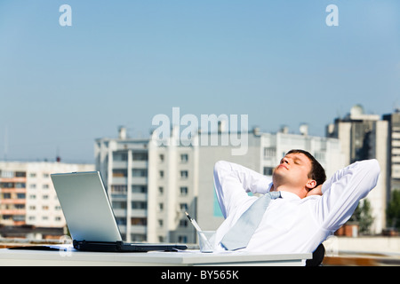 Bild des entspannten Menschen sitzen am Tisch mit Händen hinter dem Kopf und geschlossenen Augen Stockfoto