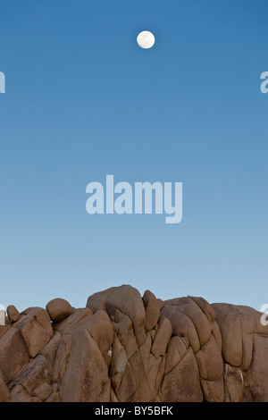 Vollmond schwebt über surreale Granit Felsformationen in der Abenddämmerung in Joshua Tree Nationalpark, Kalifornien, USA. Stockfoto