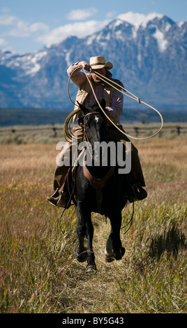 Cowboy auf Pferd mit Lasso, verschneiten Teton Bergkette in der Ferne Stockfoto