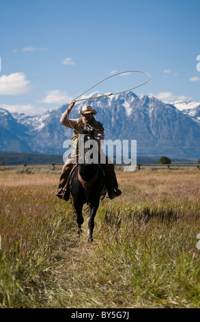 Cowboy auf Pferd mit Lasso, verschneiten Teton Bergkette in der Ferne Stockfoto