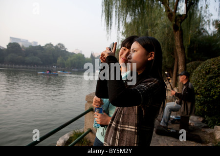 Mädchen im Teenageralter fotografieren neben See in Luxon Park, Shanghai, China Stockfoto