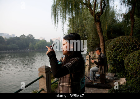 Mädchen im Teenageralter fotografieren neben See in Luxon Park, Shanghai, China Stockfoto