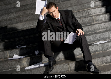 Porträt von traurigen Geschäftsmann auf Treppen mit Papieren in Händen und verlorene Ausdruck auf seinem Gesicht sitzen Stockfoto