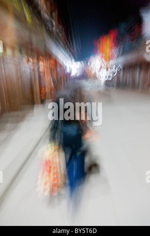 Abstrakte Aufnahme Frau mit Einkaufstüten entlang gepflasterten Straße in Stadt von Huanglongxi, Sichuan, China in der Nacht. JMH4374 Stockfoto