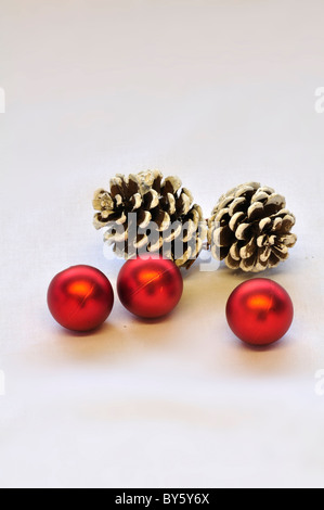 Drei rote Christbaumkugeln und zwei Zapfen auf weißem Hintergrund. UK Dezember 2010 Stockfoto