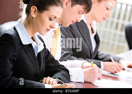 Business-Leute mit ernsten Gesichtern etwas auf dem Papier zu schreiben Stockfoto