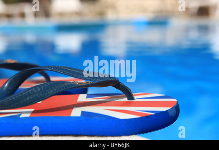 Flip Flops neben einem Schwimmbad mit einer britischen Union Jack-Flagge bedruckt Stockfoto