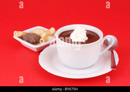 Tasse heiße Schokolade mit Sahne und ein paar Kekse serviert. Studio shot über rotem Grund. Stockfoto