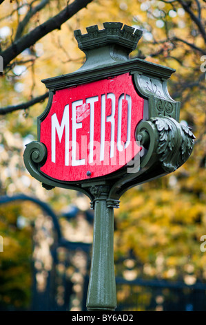 Paris Paris France / PARIS, Frankreich — ein verziertes grünes, gusseisernes Paris Metro-Schild mit roter und weißer Tafel und einer unverwechselbaren zrenelierten Spitze markiert den Eingang zu einer U-Bahn-Station. Dekorative Scrollarbeiten entlang des Rahmens sind charakteristisch für die historische städtische Infrastruktur der Stadt. Der Hintergrund zeigt verschwommenes Herbstlaub, was auf einen regnerischen Tag in der Stadt hindeutet. Diese klassischen Schilder bleiben ein dauerhaftes Symbol des Pariser öffentlichen Verkehrssystems, das von der Régie Autonome des Transports Parisiens (RATP) betrieben wird. Stockfoto