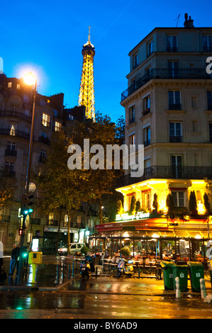 Eiffelturm Nachtszene Brasserie Le Champ de Mars Wet Streets Paris Frankreich // PARIS, Frankreich – der ikonische Eiffelturm leuchtet bei Dämmerung hell, seine goldenen Lichter reflektieren auf den nassen Straßen in der Nähe der Brasserie Le Champ de Mars im 7. Arrondissement von Paris. Warme Lichter erstrahlen aus der Brasserie, die den Sitzbereich im Freien erhellen und das lebhafte Abendambiente verstärken. Der Eiffelturm wurde 1889 fertiggestellt und ist ein 330 Meter (1.083 Fuß) hoher, schmiedeeiserner Gitterturm, der von Gustave Eiffel für die Weltausstellung 1889 entworfen wurde. Das 7. Arrondissement ist ein wohlhabender Stadtteil von Paris, bekannt Stockfoto