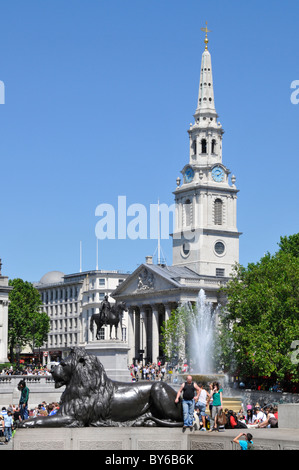 Touristen neben dem Brunnenwasser und dem monumentalen Bronzelöwen auf dem Trafalgar Square mit der anglikanischen St. Martin-in-the-Fields-Kirche und dem Turm London UK Stockfoto