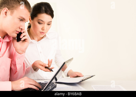 Foto von ernster Mann Telefongespräch während sein Partner zeigen ihn etwas am Laptop-Monitor während der Sitzung Stockfoto