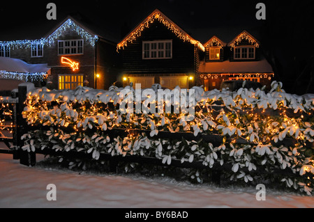 Schneebedeckte Vorgarten Lorbeer Hecke Winter Szene weiß Weihnachten Lichter Dekorationen und Illuminationen auf Haus Giebel Ende hinter Essex England GB Stockfoto