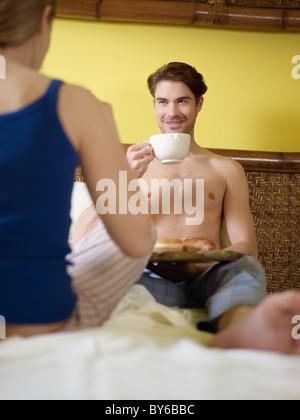 Kaukasische Heterosexuelles Paar Croissant Essen und trinken Kaffee im Bett. Vertikale Form, Rückansicht, Fokus auf Hintergrund Stockfoto