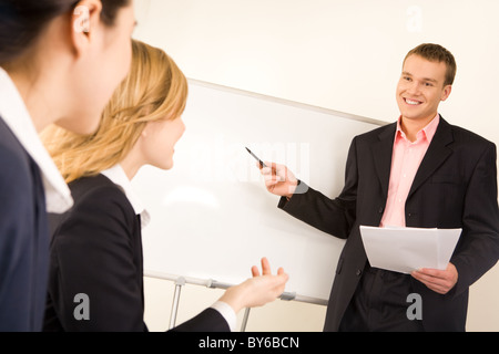 Foto von erfolgreicher Geschäftsmann am Whiteboard während zwei Damen, die ihn ansah, während Seminars stehen Stockfoto