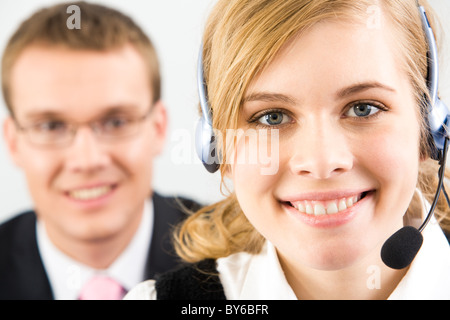 Gesicht der hübschen Sekretärin tragen Kopfhörer auf Hintergrund der zuversichtlich Geschäftsmann Stockfoto