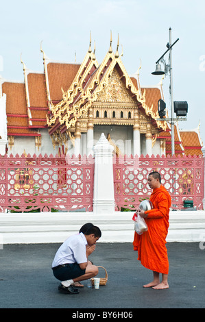 Zwei Menschen vor einem Mönch zu beten, nachdem sie, Himalms vor Wat Benjamabophit, Bangkok, Thailand gegeben hatte Stockfoto