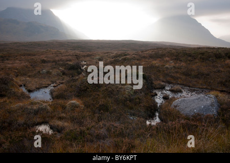 Einen dramatischen Blick auf die Sonne bricht durch die Wolken auf einem herbstlichen Moor in den Highlands von Schottland. Stockfoto