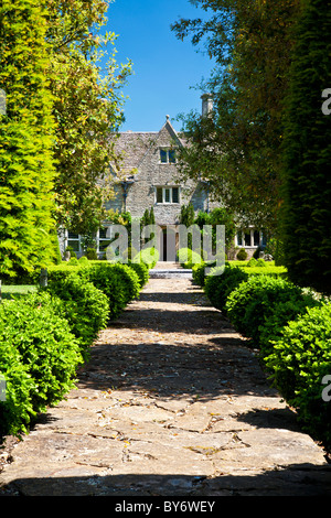 Ein gepflasterter Weg eingefasst mit Box Hecke führt bis vor die Haustür von einem großen englischen Herrenhaus im Sommer Stockfoto