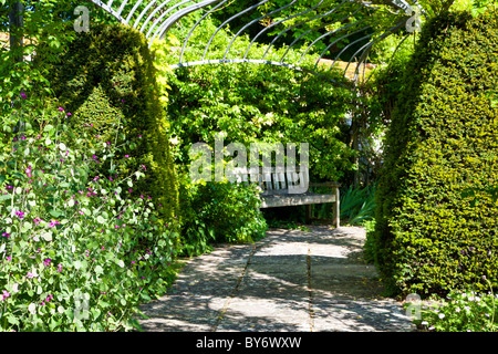Holzsitz oder Bank in einer schattigen Ecke unter einer Pergola in einem englischen Landhaus-Garten im Sommer. Stockfoto