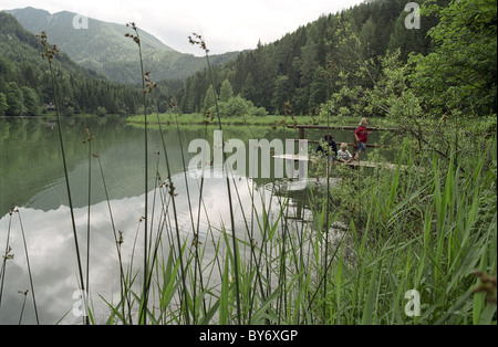Eine Mutter mit zwei Kindern sitzen auf einer hölzernen Plattform an einem See, Schaffner Weiher, Stodertal, Österreich, Alpen, Europa Stockfoto
