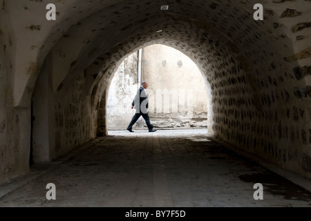 Ein türkischer Mann in einem Geschäftsanzug, der in der historischen und alten Stadt Urfa, im Südosten Anatoliens, in der Türkei, eine Gasse hinuntergeht. Stockfoto