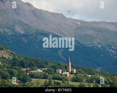 Gleitschirmflieger über ein kleines Dorf in den französischen Alpen, geschossen von Embrun, Hautes Alpes, Frankreich Stockfoto