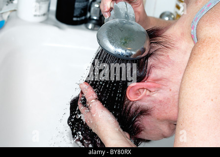 Frau Spülung haar über einer Badewanne nach Anwendung von Haarfärbemitteln uk Stockfoto