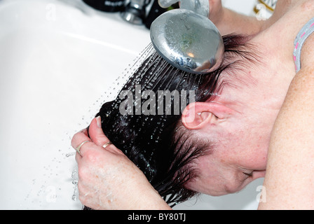 Frau Spülung haar über einer Badewanne nach Anwendung von Haarfärbemitteln uk Stockfoto