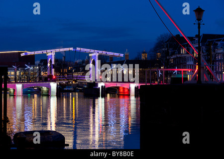 Die Magere Brug oder Skinny Bridge ist ein Wahrzeichen von Amsterdam. An der Amstel in der Dämmerung im Winter mit einer festlichen Beleuchtung Stockfoto