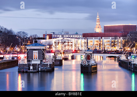 Amsterdam Amstel Fluss mit Skinny Bridge, Magere Brug und Muziektheater, Opernhaus in der Dämmerung im Winter. Stockfoto