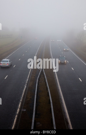 Fahrzeuge fahren entlang einer Autobahn an einem nebeligen Tag entlang. Die Sicht ist so gering, dass sie ihre Scheinwerfer eingeschaltet haben. Stockfoto